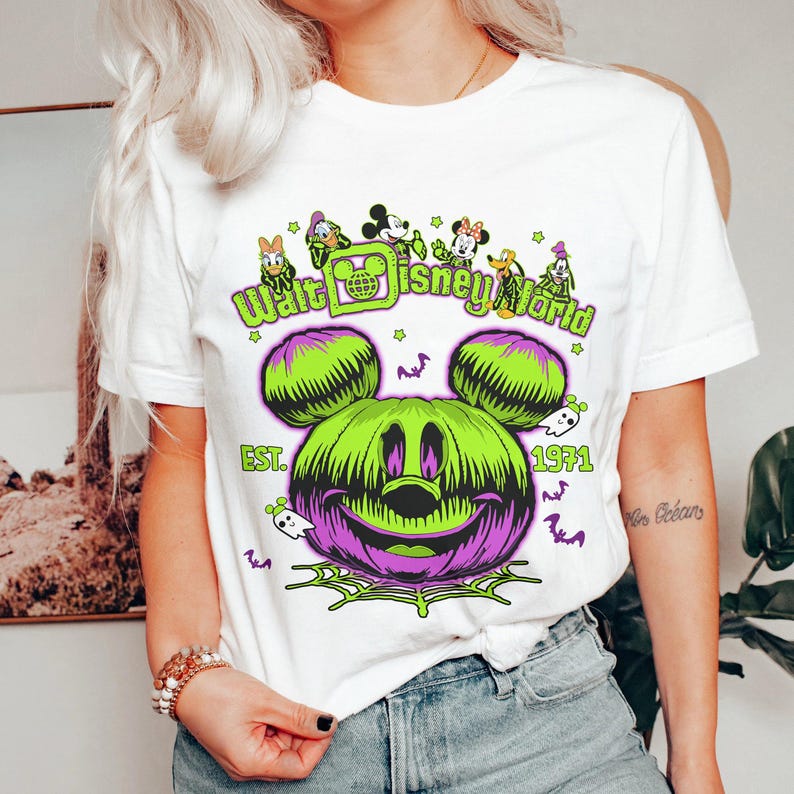 May include: White t-shirt featuring a Halloween-themed Walt Disney World design. The graphic includes a green and purple Mickey Mouse pumpkin, the text "Walt Disney World", and the year "1971". Additional characters and spooky elements are also present.