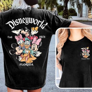 May include: Black t-shirt featuring a Disney World graphic with Mickey Mouse, Minnie Mouse, Donald Duck, Daisy Duck, Goofy, and Pluto. The text "Disneyworld Est 1971 Florida" is also printed on the shirt.