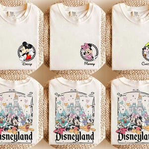 May include: Off-white t-shirts with Disney character graphics. Some shirts feature Mickey Mouse, Minnie Mouse, and Goofy in circular designs with text like "Daddy," "Mommy," and "Custom Name." Other shirts display a Disneyland graphic.