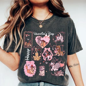 May include: Dark gray t-shirt featuring a Valentine's Day design with cartoon dogs. The design includes the words "Happy Valentine's Day" and various dog characters in pink frames and heart shapes. The shirt has a vintage, worn look.