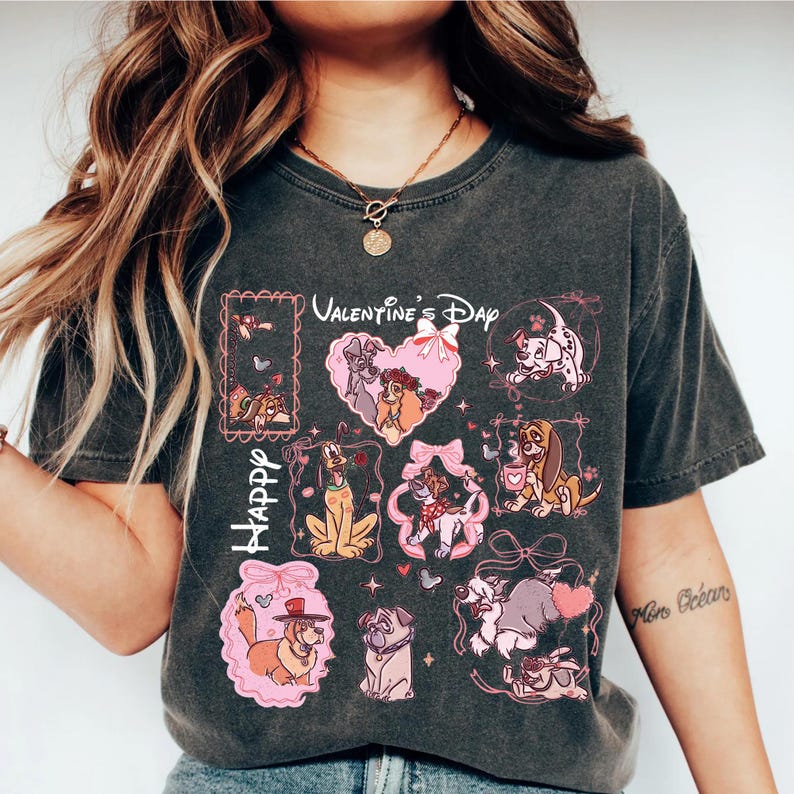 May include: Dark gray t-shirt featuring a Valentine's Day design with cartoon dogs. The design includes the words "Happy Valentine's Day" and various dog characters in pink frames and heart shapes. The shirt has a vintage, worn look.