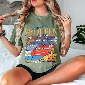 May include: Green t-shirt with a graphic of Lightning McQueen and other cars from the Cars movie. The text "Lightning McQueen" and "Think Fast" are printed on the shirt.