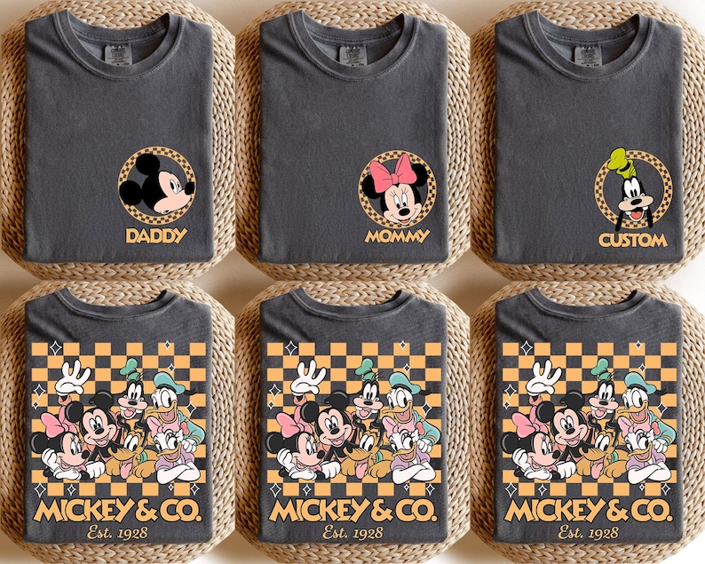 May include: Three gray t-shirts with a checkered pattern and Mickey Mouse characters. The shirts have the text "Mickey & Co. Est. 1928" printed on the bottom. The shirts are labeled "Daddy", "Mommy", and "Custom".