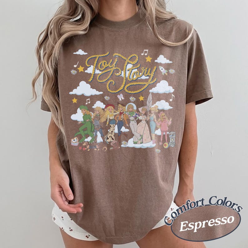 May include: A brown short-sleeve t-shirt featuring a graphic print with the text Toy Story in yellow rope-style lettering. The design includes white clouds, yellow stars, and a group of illustrated characters from the Toy Story film franchise.