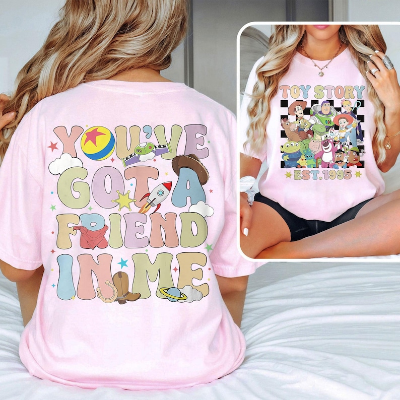 May include: Pink t-shirt with a colorful graphic that says "You've got a friend in me" and features characters from the Toy Story movie franchise. The back of the shirt has a black and white checkered graphic with the text "Toy Story Est. 1995".