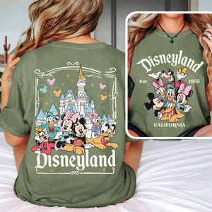 May include: Green t-shirt with a graphic of Mickey Mouse and friends in front of Sleeping Beauty's castle. The text "Disneyland Est. 1955 California" is printed on the shirt.