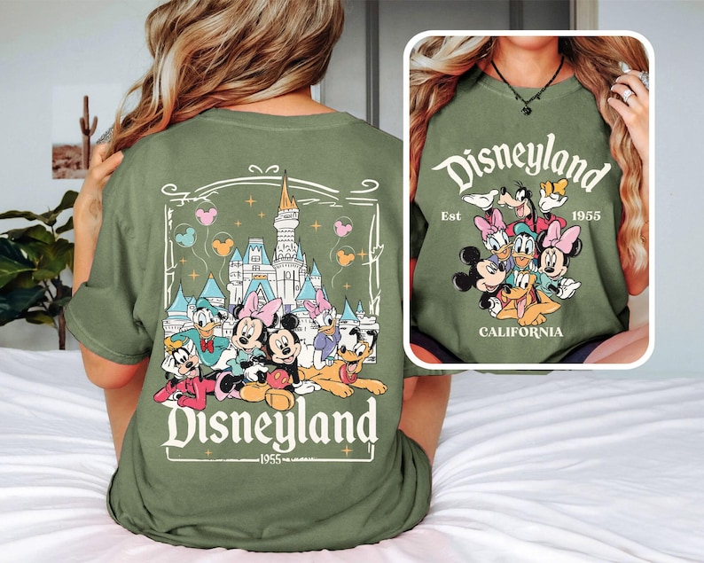 May include: Green t-shirt with a graphic of Mickey Mouse and friends in front of Sleeping Beauty's castle. The text "Disneyland Est. 1955 California" is printed on the shirt.