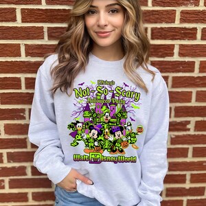 May include: A light gray sweatshirt featuring a Halloween-themed graphic. The design includes the text "Mickey's Not-So-Scary Halloween Party" with Disney characters in costume, and the words "Walt Disney World".