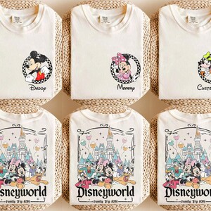 Puede incluir: Camisetas de color crema con dise&ntilde;os de personajes de Disney. Algunas camisetas presentan a Mickey Mouse, Minnie Mouse y Goofy con textos como "Daddy", "Mommy" y "Custom Name". Otras camisetas muestran un gr&aacute;fico de Disneyworld con personajes y el texto "Family Trip 2020."