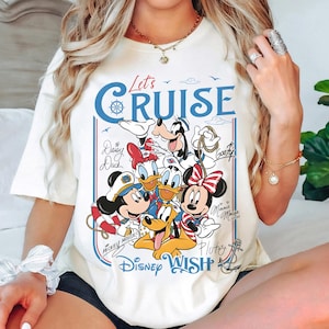 May include: Cream-colored t-shirt featuring a graphic of Disney characters, including Mickey Mouse, Minnie Mouse, Donald Duck, and Goofy. The design includes the text "Let's Cruise" and "Disney Wish" in blue and red.