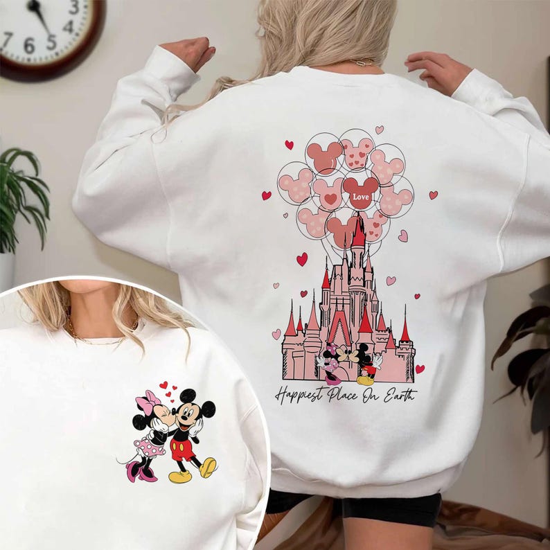 May include: White sweatshirt featuring a graphic of Mickey and Minnie Mouse kissing. The back of the sweatshirt has a castle design with Mickey Mouse balloons and the words "Happiest Place On Earth."