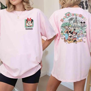 Puede incluir: Camiseta rosa claro con Minnie Mouse y la palabra "Custom" en la parte delantera. La parte trasera de la camiseta muestra un gr&aacute;fico colorido de personajes de Disney y las palabras "Walt Disney World".