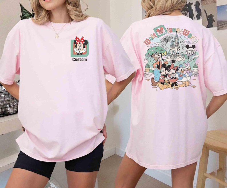 Puede incluir: Camiseta rosa claro con Minnie Mouse y la palabra "Custom" en la parte delantera. La parte trasera de la camiseta muestra un gr&aacute;fico colorido de personajes de Disney y las palabras "Walt Disney World".