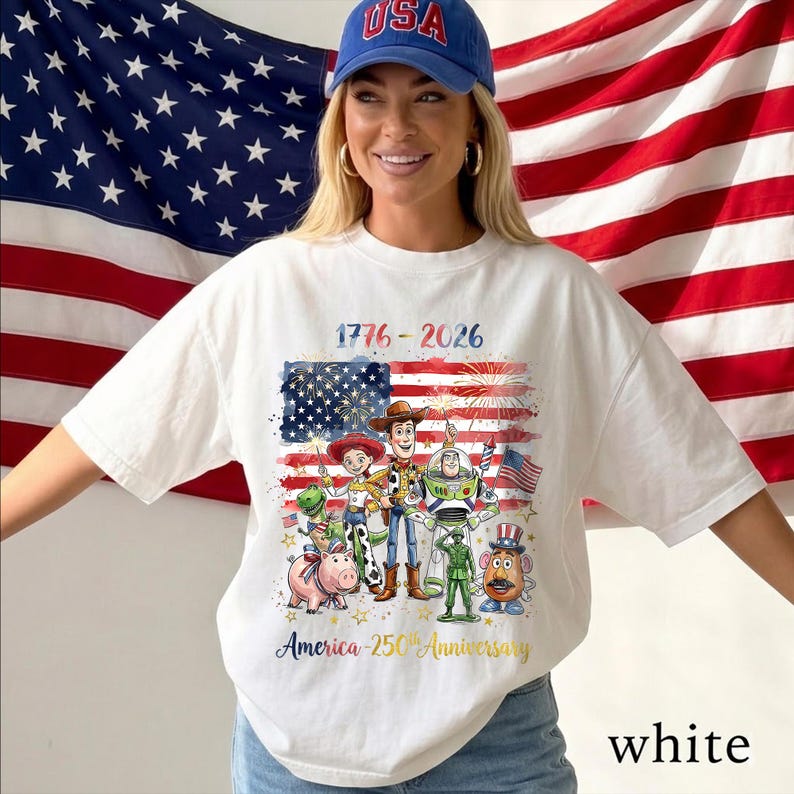 May include: A white t-shirt featuring a graphic of Toy Story characters including Woody, Buzz Lightyear, Jessie, Rex, Hamm, Mr. Potato Head, and a green army soldier. The text reads 1776-2026 and America 250th Anniversary with a US flag background.