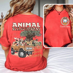 May include: Red t-shirt with a graphic of a brown jeep with Disney characters and the text "ANIMAL KINGDOM" and "Wild about Disney". A smaller image shows a Daisy Duck graphic with the text "Custom Name".