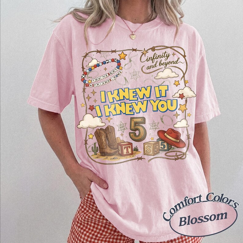 May include: A light pink short-sleeve t-shirt featuring a graphic print with a lasso border, cowboy boots, a red hat, alphabet blocks, and the text "Cinfinity and beyond", "You've got a friend in me", "I KNEW IT I KNEW YOU", and the number 5.