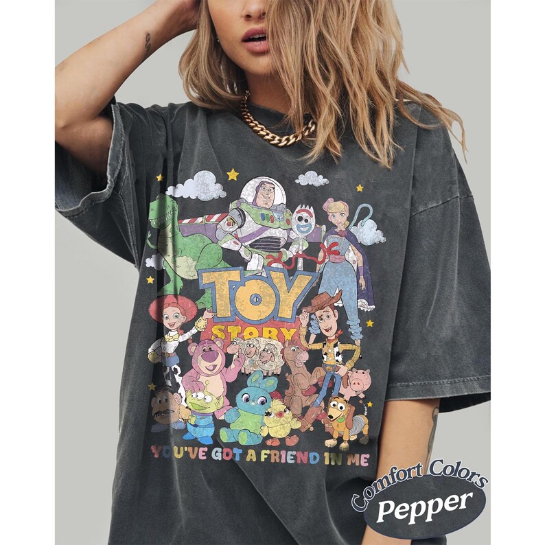 May include: A charcoal gray short-sleeve t-shirt featuring a vintage-style graphic print of Toy Story characters including Woody, Buzz Lightyear, and Jessie. The text reads Toy Story and You've Got A Friend In Me. The shirt has a faded, washed-out appearance.