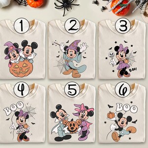 May include: Six cream-colored t-shirts with Halloween-themed Mickey and Minnie Mouse graphics. Each shirt features a different design, including Mickey and Minnie with pumpkins, witch hats, and the word "BOO!" in various styles. The designs are in shades of orange, purple, black, and white.