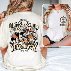 May include: Cream-colored t-shirt featuring a graphic of Disney characters, including Mickey and Minnie Mouse, Donald Duck, and Goofy, with the text "Mickey's Not-So-Scary Halloween Party 2026". The shirt also has a smaller graphic of Pluto.