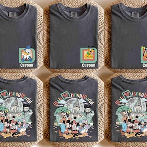Puede incluir: Seis camisetas de color gris oscuro, dobladas sobre esteras tejidas. Tres camisetas presentan gr&aacute;ficos de personajes de Disney con la palabra "Custom". Las otras tres camisetas muestran un dise&ntilde;o colorido de "Walt Disney World" con personajes de Disney.