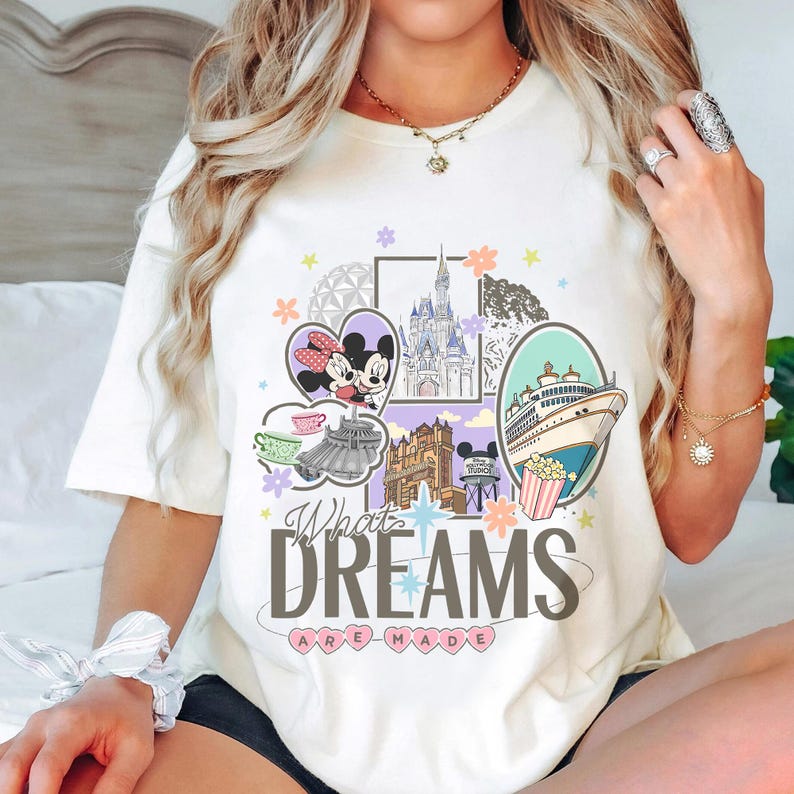 May include: Cream-colored t-shirt featuring a colorful graphic with Minnie and Mickey Mouse, a castle, and a cruise ship. The text "What Dreams Are Made" is displayed in a stylized font. The design includes pastel colors and floral accents.