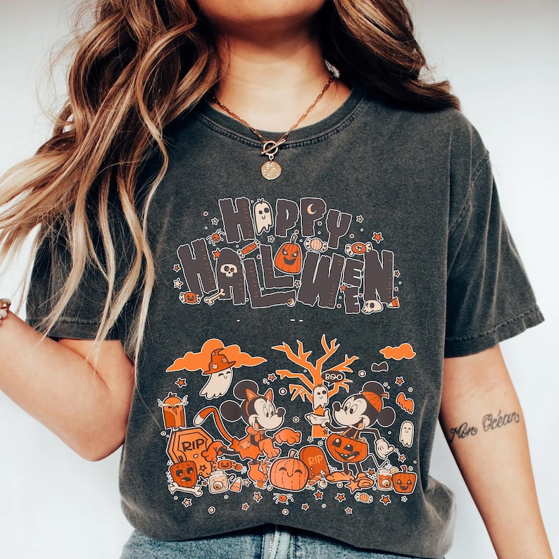 Puede incluir: Camiseta gris oscuro con las palabras "Happy Halloween" en naranja y blanco. La camiseta presenta personajes de dibujos animados, calabazas, fantasmas y otros gr&aacute;ficos tem&aacute;ticos de Halloween. Un dise&ntilde;o divertido y festivo para la temporada de miedo.