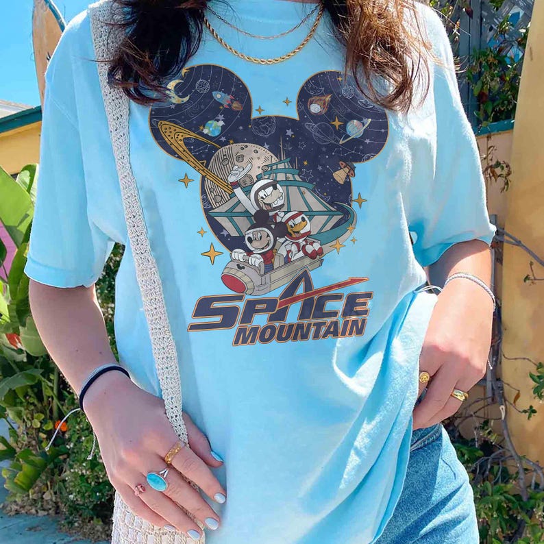 May include: A light blue t-shirt with a graphic of Mickey Mouse and friends riding a spaceship in a galaxy setting. The text "Space Mountain" is printed below the graphic.