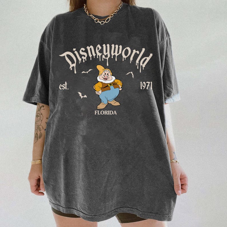 Op de afbeelding: Donkergrijs T-shirt met een Disneyworld-afbeelding. Het ontwerp bevat de tekst "Disneyworld", het jaar "1971" en een cartoonfiguur. Het woord "Florida" staat ook op het shirt.