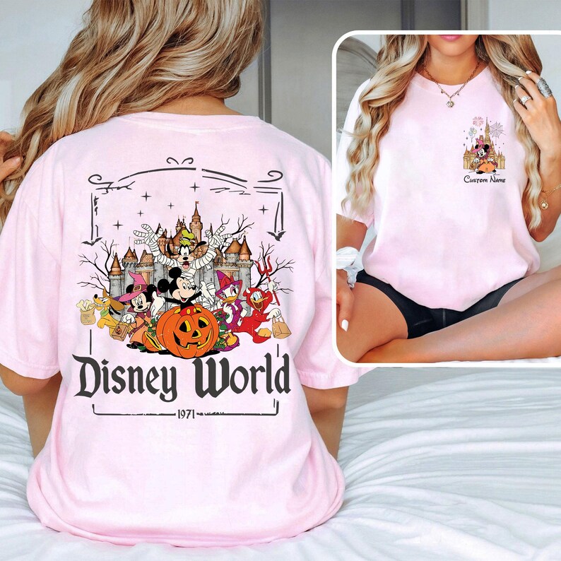 May include: Light pink t-shirt featuring a Disney World Halloween design. The graphic includes Mickey Mouse, Minnie Mouse, Donald Duck, and Goofy, with a pumpkin and castle. The text "Disney World" and "1971" are also visible.
