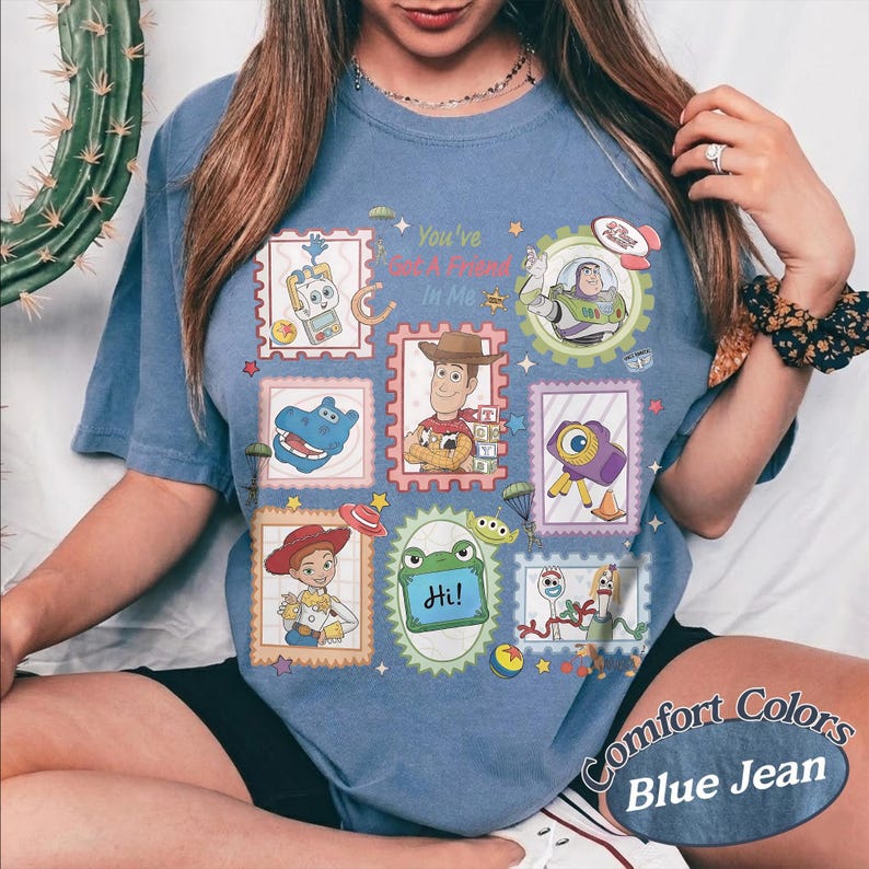 May include: A blue short-sleeve t-shirt featuring a graphic print of various Toy Story characters arranged in postage stamp-style frames. The design includes Woody, Buzz Lightyear, Jessie, Forky, and other icons with the text You've Got A Friend In Me.