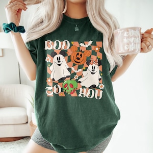 May include: Dark green t-shirt with a Halloween-themed graphic. The design features two ghost characters, a jack-o'-lantern, and the text "BOO TO YOU" in a retro font. The shirt has a checkered background with floral accents.