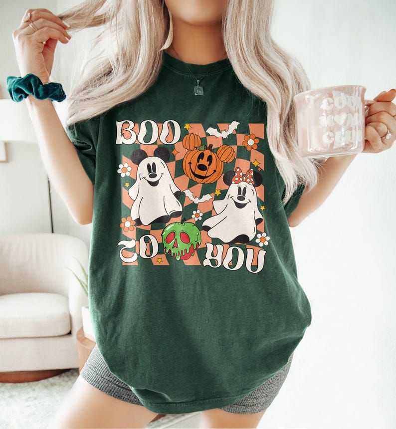 May include: Dark green t-shirt with a Halloween-themed graphic. The design features two ghost characters, a jack-o'-lantern, and the text "BOO TO YOU" in a retro font. The shirt has a checkered background with floral accents.