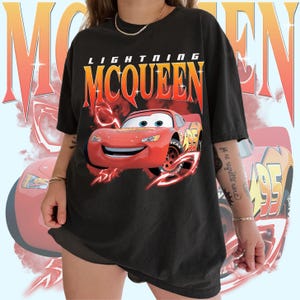 May include: Black oversized t-shirt featuring a red cartoon race car with the text "Lightning McQueen" in red and yellow letters.