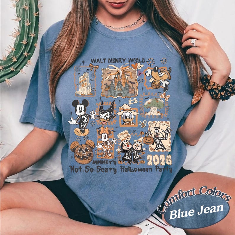 Pu&ograve; includere: T-shirt blu jeans con una grafica raffigurante personaggi Disney in costume di Halloween. La maglietta include il testo "Walt Disney World", "Mickey's Not-So-Scary Halloween Party 2026" e "Comfort Colors Blue Jean".