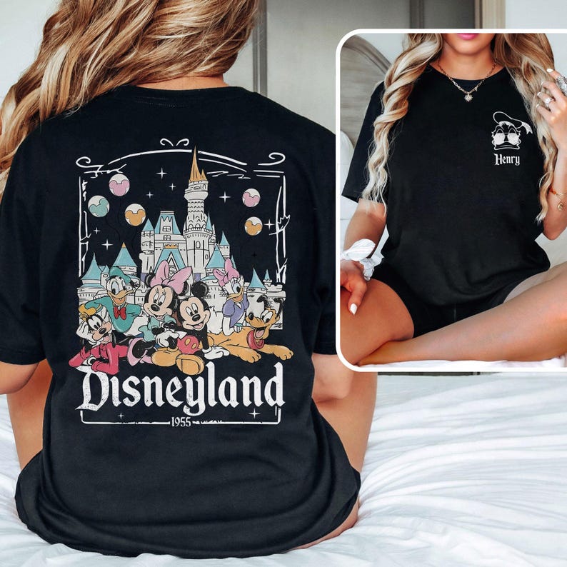 K&ouml;nnte beinhalten: Schwarzes T-Shirt mit einem Aufdruck von Mickey Mouse und seinen Freunden vor dem Disneyland-Schloss. Der Text "Disneyland - 1955" ist unter dem Aufdruck gedruckt.