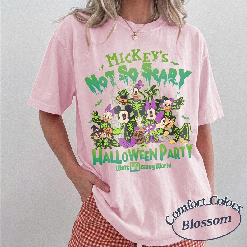 Op de afbeelding: Zachtroze T-shirt met een Halloween-thema Disney-afbeelding. Het ontwerp toont verschillende personages in kostuums, met de tekst "Mickey's Not So Scary Halloween Party" en "Walt Disney World" in het groen. Het shirt is gelabeld "Comfort Colors Blossom".