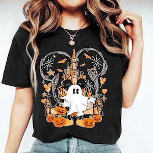 May include: Black t-shirt with a Halloween design. The graphic features a castle, a ghost, pumpkins, and Mickey Mouse ears. The design uses orange, white, and black, with fireworks and bats. This casual t-shirt is suitable for Halloween.