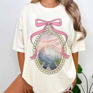 May include: A white t-shirt with a pink bow and a vintage illustration of a sphere with a star pattern inside a pearl-encrusted frame.