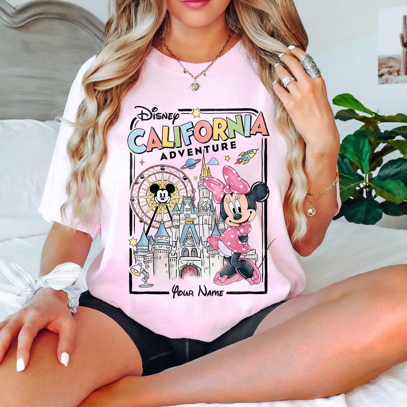Puede incluir: Camiseta rosa claro con un gr&aacute;fico colorido de Minnie Mouse y Mickey Mouse frente a un castillo y una noria. El texto "Disney California Adventure" se muestra encima del gr&aacute;fico. La camiseta es de color rosa claro.