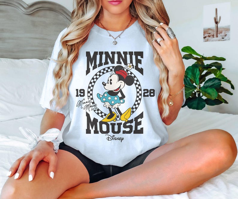 Op de afbeelding: Een wit T-shirt met een zwart-witte afbeelding van Minnie Mouse. De afbeelding bevat de tekst "Minnie Mouse" en "Disney".