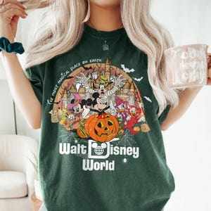 May include: Green t-shirt with a Halloween-themed graphic of Mickey Mouse and friends in front of Cinderella's Castle. The text "The Most Magical Place on Earth" and "Walt Disney World" are printed on the shirt.