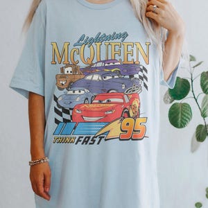 May include: Light blue t-shirt with a graphic of Lightning McQueen and other Cars characters. The graphic includes the text "Lightning McQueen", "Think Fast", and "95".