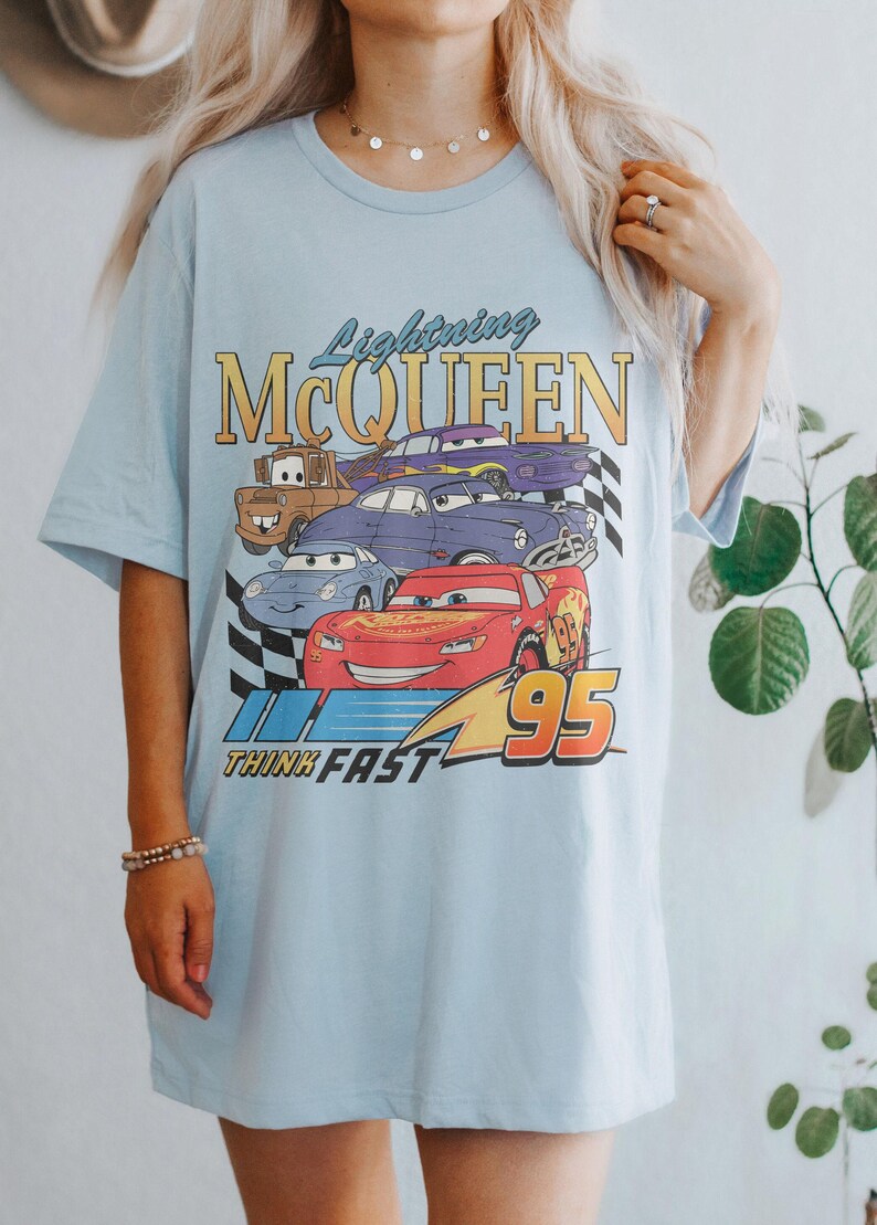May include: Light blue t-shirt with a graphic of Lightning McQueen and other Cars characters. The graphic includes the text "Lightning McQueen", "Think Fast", and "95".