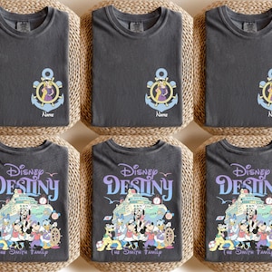May include: Six dark gray t-shirts. The top row features an anchor design with a character and the name "Name". The bottom row displays "Disney Destiny" with a cruise ship and characters, and "The Smith Family".