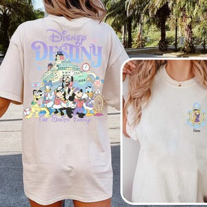 May include: Beige t-shirt featuring a colorful graphic of Disney characters on a cruise ship with the text "Disney Destiny" and "The Smith Family 2026". A smaller image on the front shows an anchor with a character and the word "Name".
