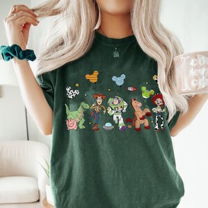 Puede incluir: Camiseta verde oscuro con un gr&aacute;fico colorido de personajes de Toy Story, incluyendo a Woody y Buzz Lightyear. El dise&ntilde;o incluye globos y una nave espacial. La camiseta est&aacute; hecha de un material suave.