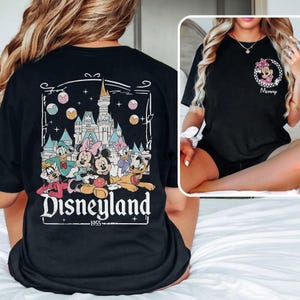 May include: Black t-shirt with a graphic of Mickey Mouse and friends in front of Sleeping Beauty's castle. The text "Disneyland" and "1955" are printed below the graphic.