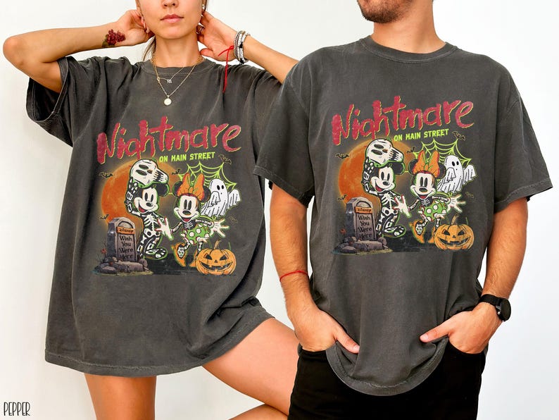 May include: Dark gray t-shirts with a Halloween-themed graphic. The design features Mickey and Minnie Mouse in skeleton costumes, a ghost, and a jack-o'-lantern, with the words "Nightmare on Main Street".
