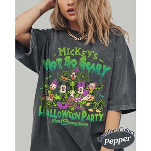 Op de afbeelding: Donkergrijs T-shirt met een Halloween-thema met Disney-personages. Het ontwerp bevat de tekst "Mickey's Not So Scary Halloween Party" en "Walt Disney World" in groen en wit. Het shirt is gelabeld "Comfort Colors Pepper".