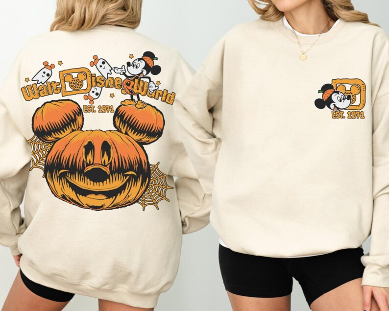 May include: Beige sweatshirt featuring a Halloween-themed Walt Disney World design. The back displays a large orange Mickey Mouse pumpkin, ghosts, and the text "Walt Disney World Est. 1971." The front has a smaller Mickey Mouse graphic. A cozy, festive apparel item.